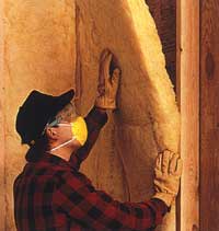 Technician installing yellow batt fiberglass insulation in a wall.