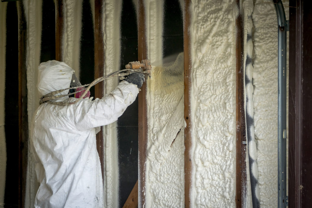 Worker spraying closed-cell spray foam insulation in a wall.