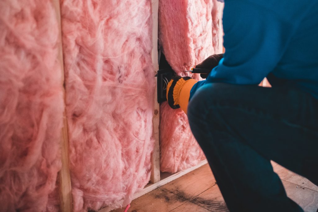Technician installing pink fiberglass batt insulation in a wall.